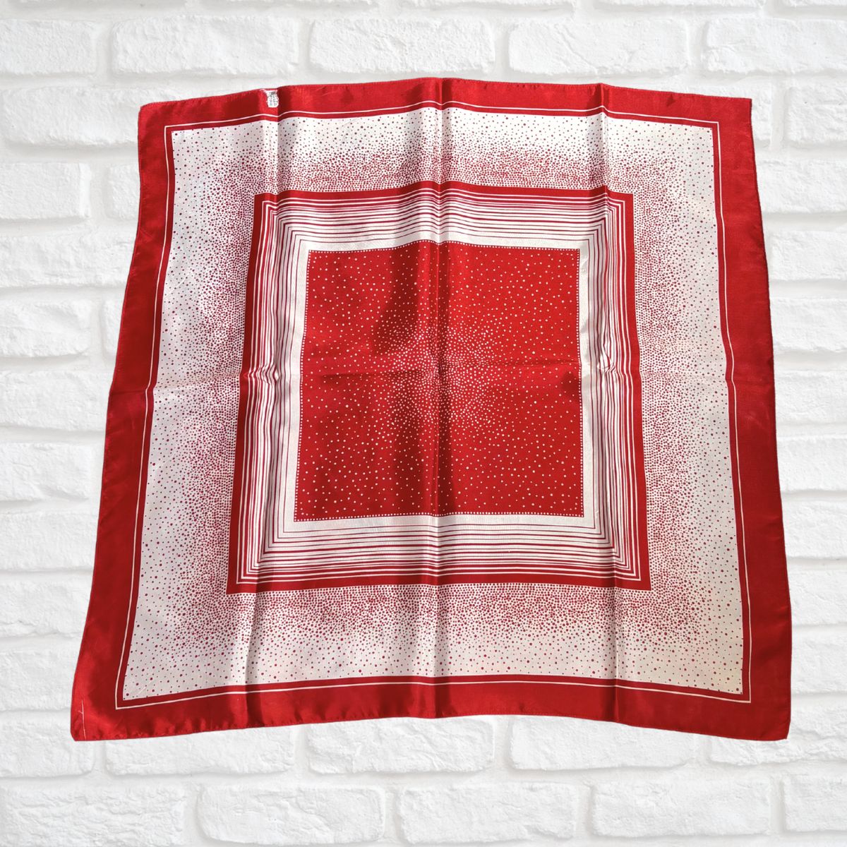 Red and white patterned square scarf on a white brick wall background