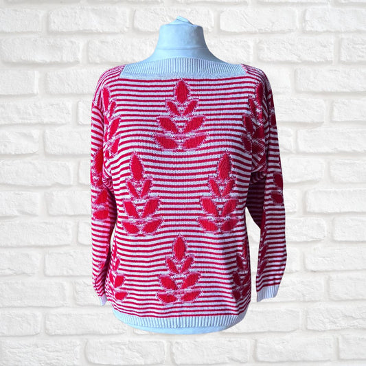 A knit sweater displayed on a mannequin torso against a white brick wall. The sweater has a light blue base with horizontal red stripes and large red leaf motifs woven throughout.