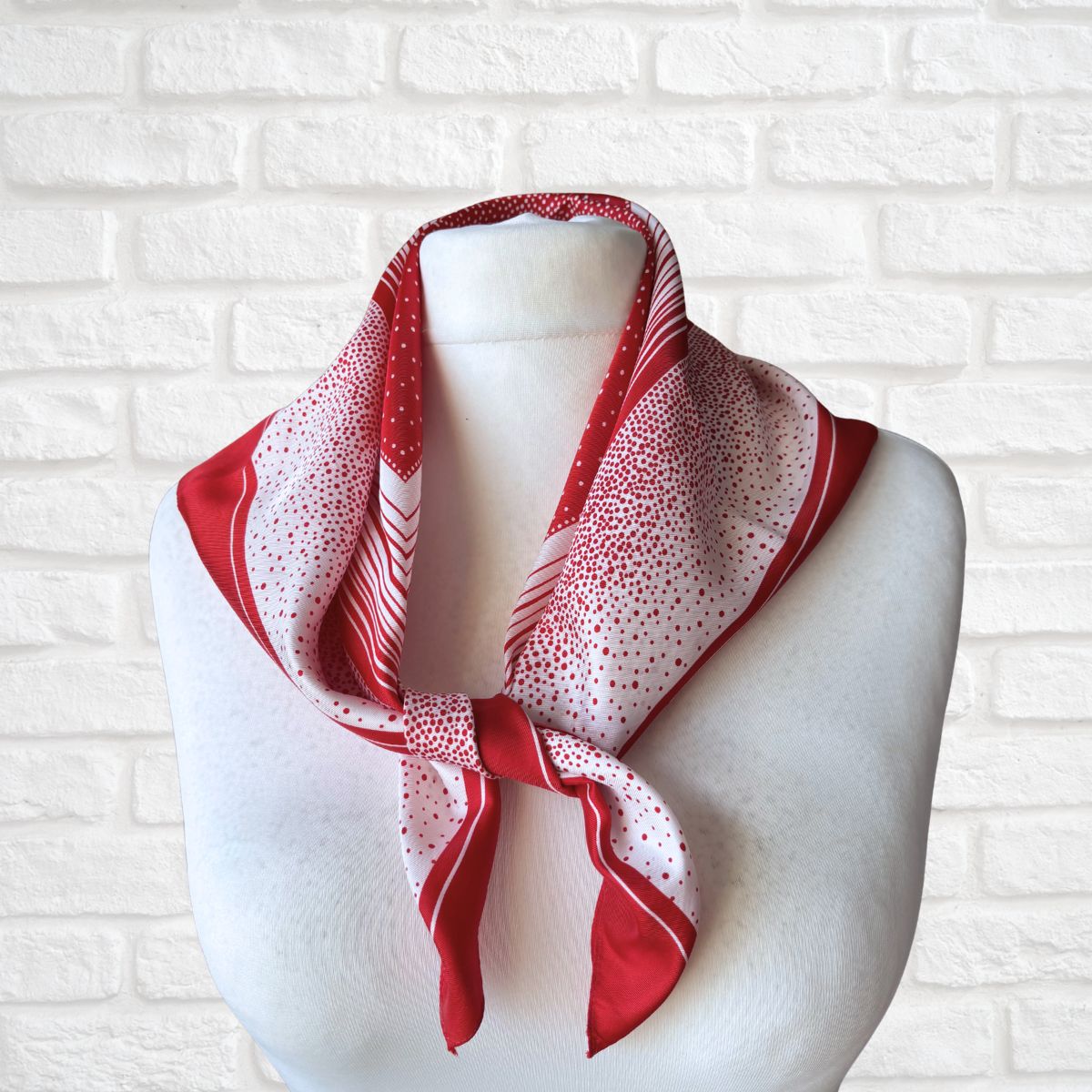 Red and white patterned scarf on a mannequin against a white brick wall.