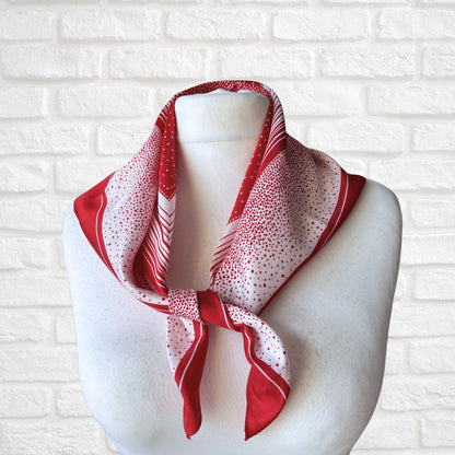Red and white patterned scarf on a mannequin against a white brick wall.