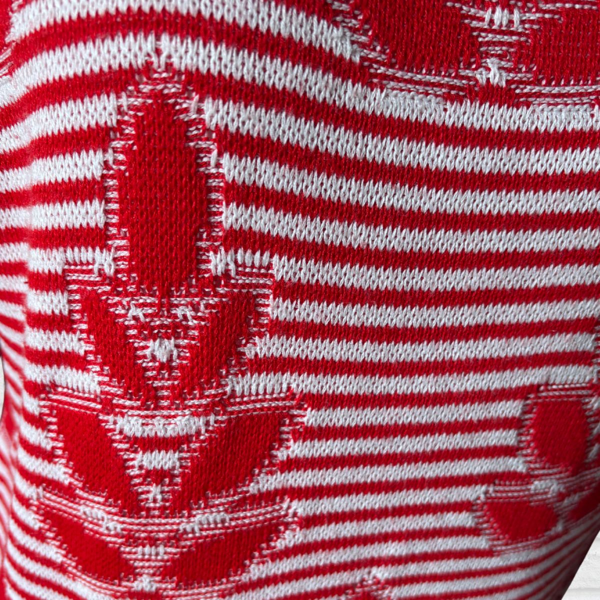 Close-up of a red and white knit fabric with horizontal stripes and a red maple leaf pattern.