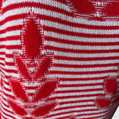 Close-up of a red and white knit fabric with horizontal stripes and a red maple leaf pattern.