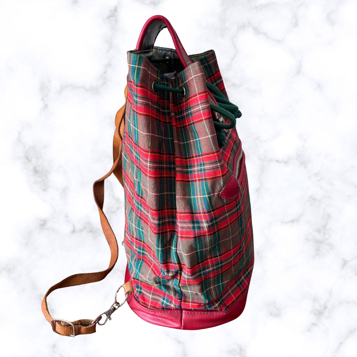 Plaid backpack with a brown strap on a white marble background