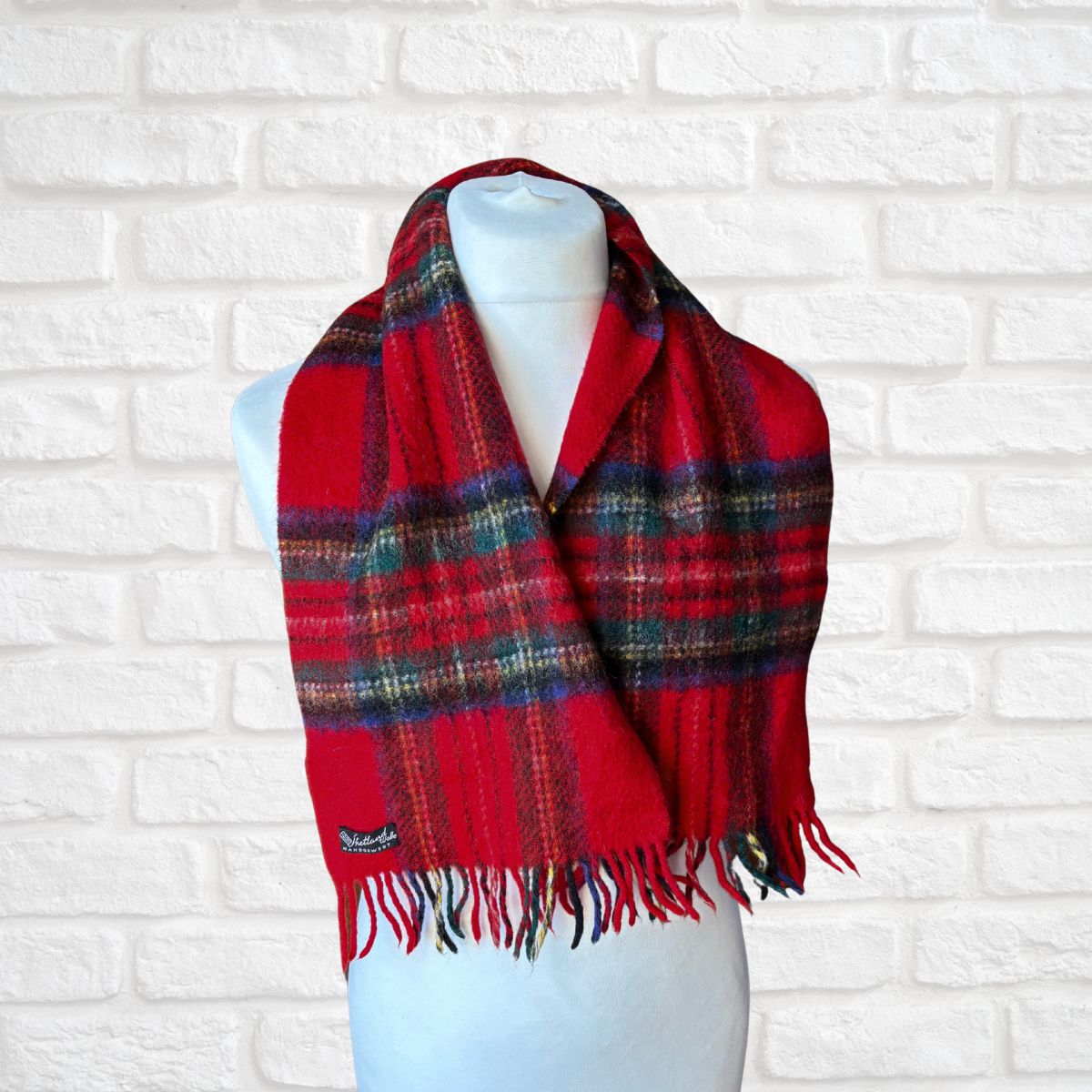 Red plaid scarf on a mannequin against a white brick wall background