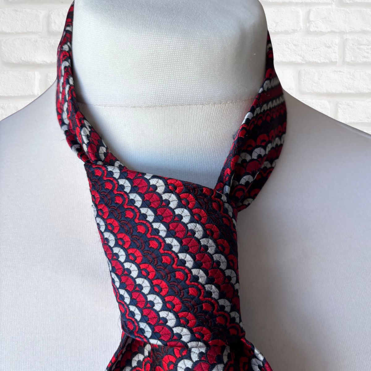 Red, white, and black patterned scarf on a mannequin against a white brick wall.