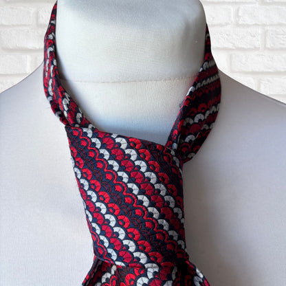 Red, white, and black patterned scarf on a mannequin against a white brick wall.