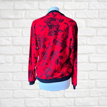 A red long-sleeve sweatshirt  with a black rose pattern, displayed on a light blue mannequin torso against a white brick wall background.