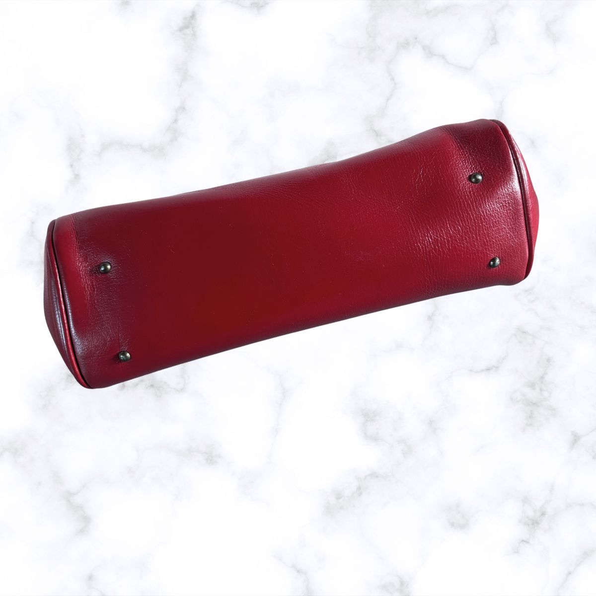 A red leather cylindrical bag with metal studs, photographed diagonally on a white marble background.