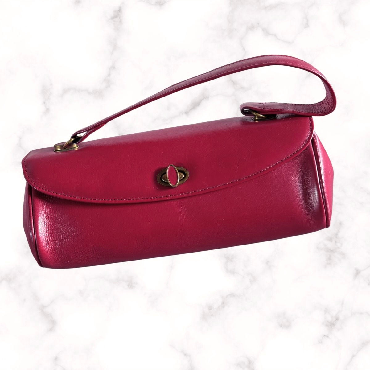 A red leather handbag with a top handle, gold-tone hardware, and a central decorative clasp, shown on a white marble background.