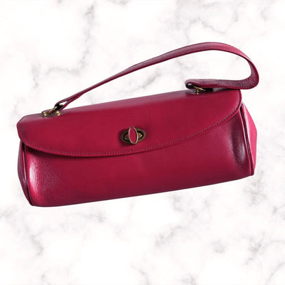 A red leather handbag with a top handle, gold-tone hardware, and a central decorative clasp, shown on a white marble background.