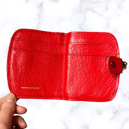 Red leather wallet held by a hand on a white background