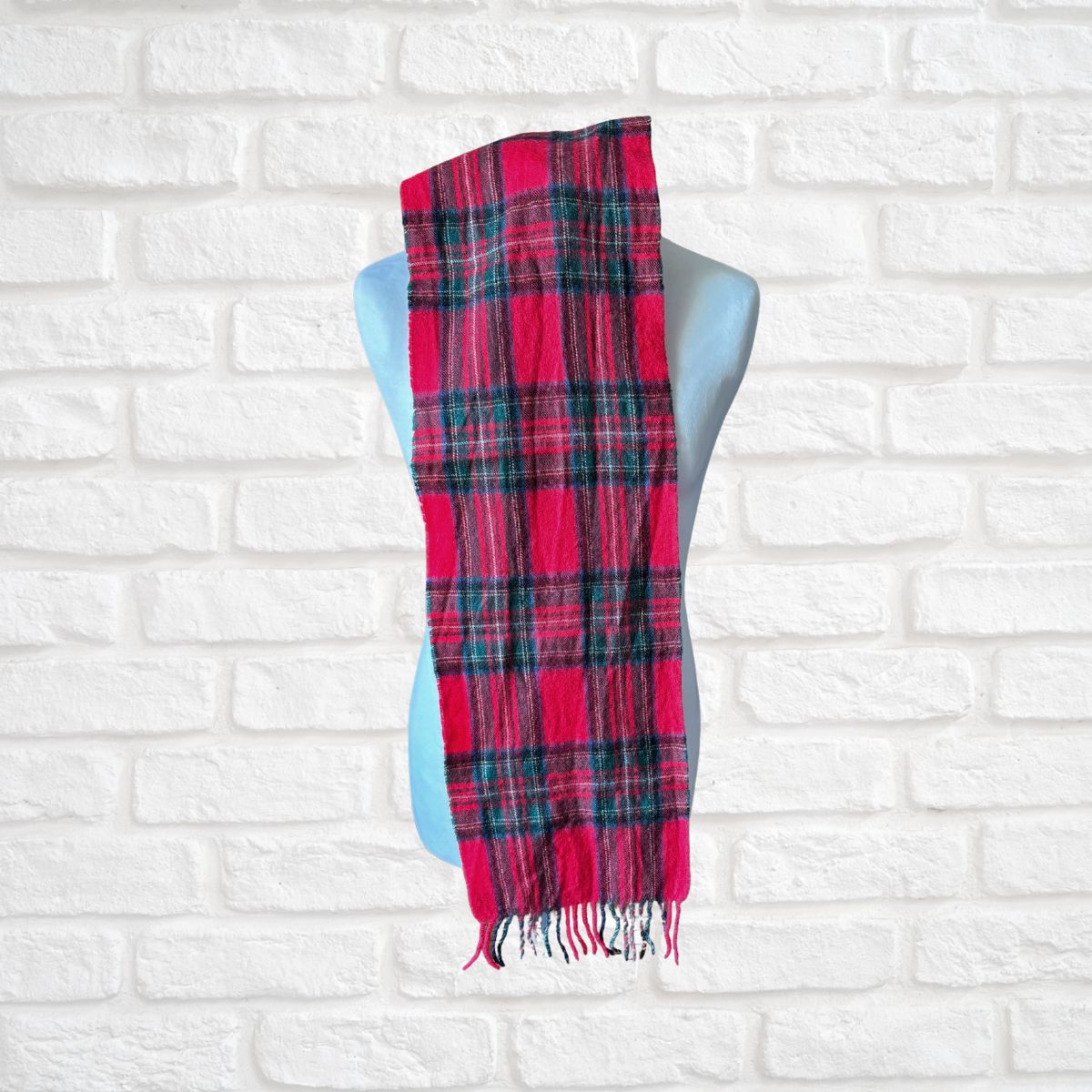Red and black plaid scarf on a mannequin against a white brick wall.