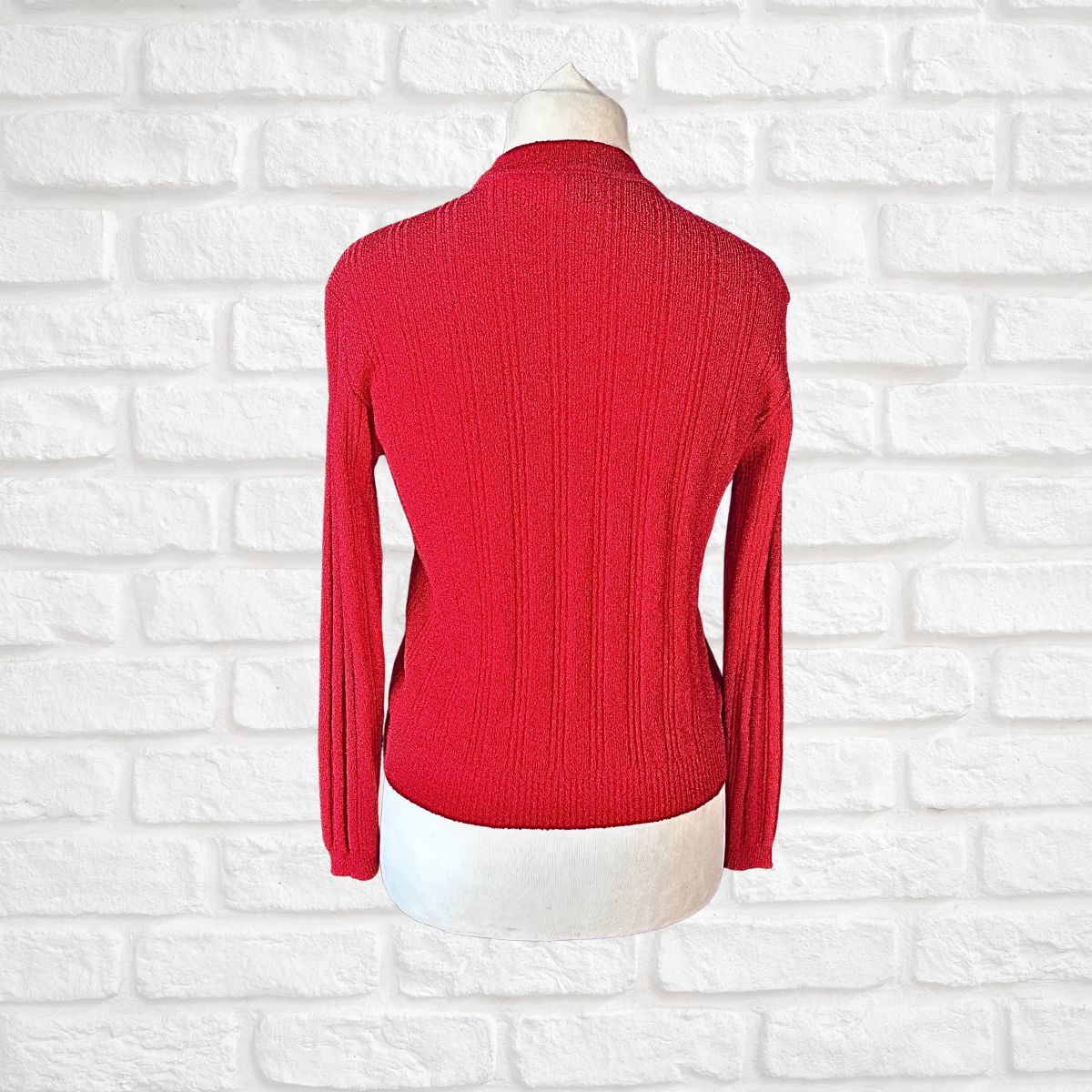 A red ribbed knit mock neck sweater displayed on a white mannequin torso against a white brick wall background.