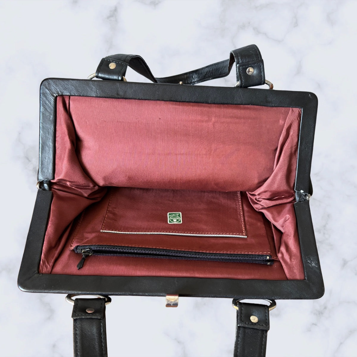 Black leather bag with red interior on a white marble background