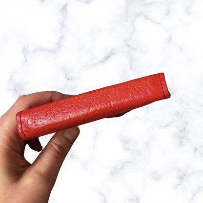 Red leather object held by a hand against a white marble background