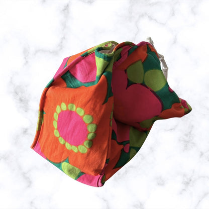 A colorful fabric pouch with a bold retro floral pattern in orange, pink, green, and yellow, displayed on a white marble background.