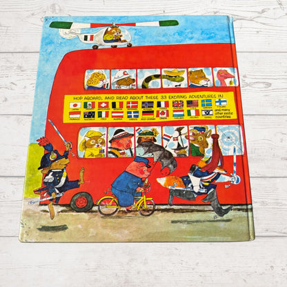 Children's book cover with a colorful illustration of a red bus and various animals on a wooden surface.