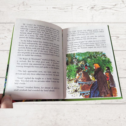 An open book spread laid flat on a white textured surface, showing printed text on both pages and a colorful illustration on the right page with a knight in armor and a woman in a blue dress.