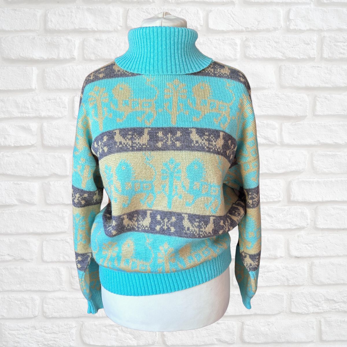 A turquoise and beige knit turtleneck sweater with a gray Nordic reindeer pattern, displayed on a white mannequin torso against a white brick wall background.