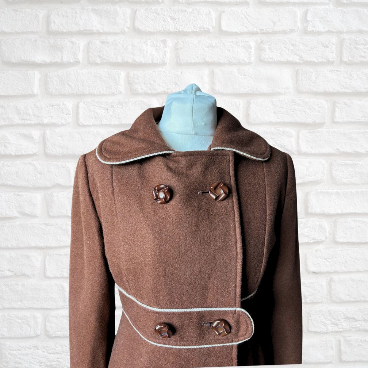 Brown coat with white trim on a mannequin against a white brick wall background