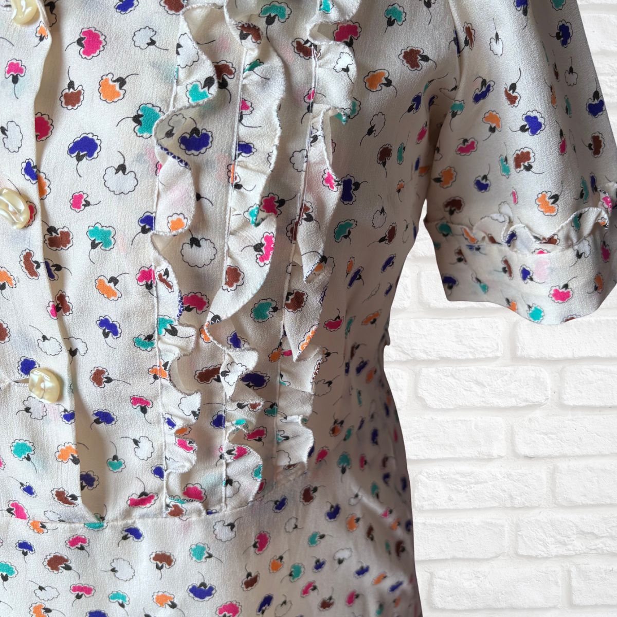 Close-up of a shirt with colorful floral pattern against a white brick wall.