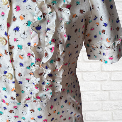 Close-up of a shirt with colorful floral pattern against a white brick wall.