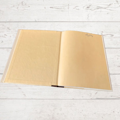 An open hardcover notebook with blank beige pages, placed flat on a white-washed wooden surface.