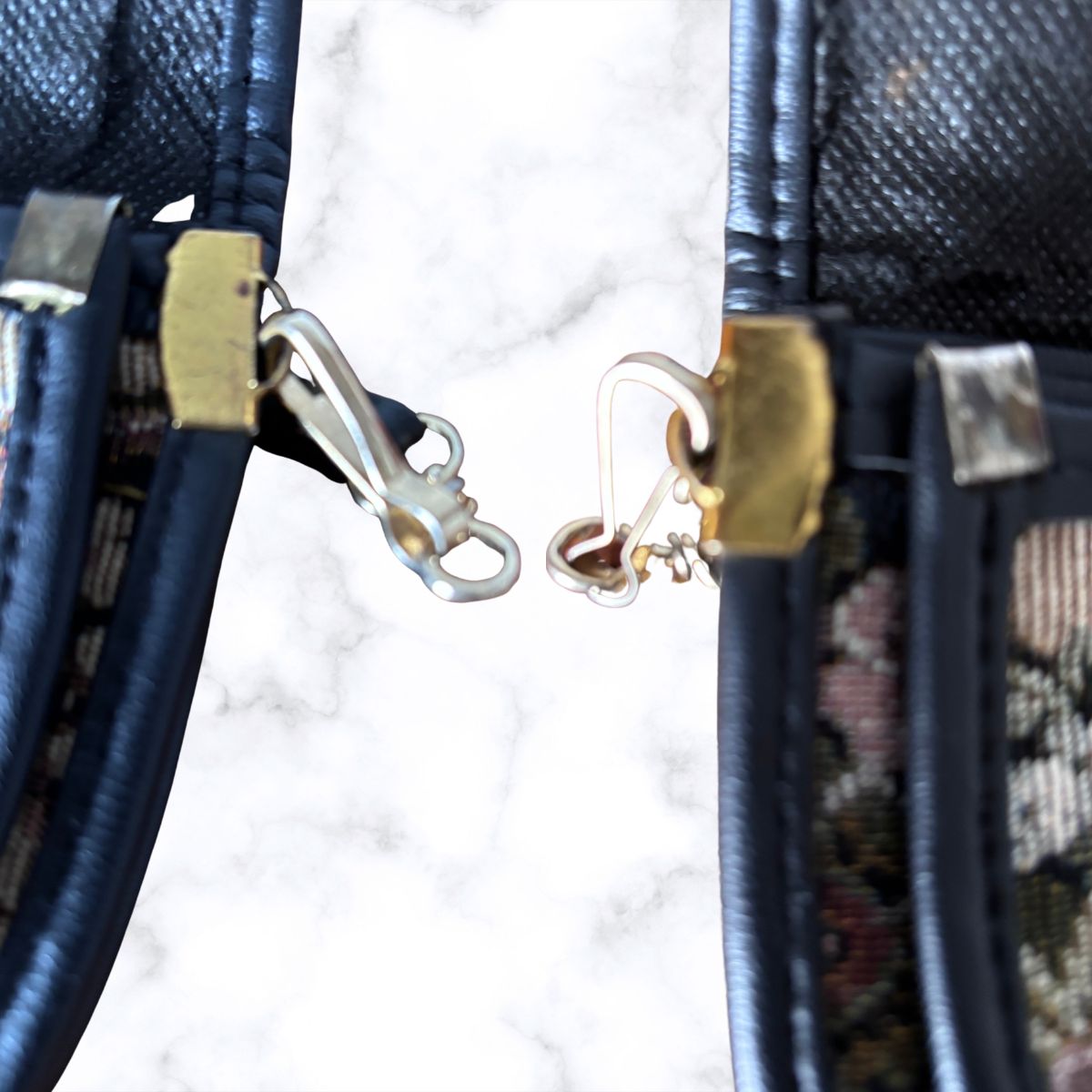 Close-up of a vintage handbag showing the side profile with gold-tone metal hardware clasp against a white marble background.