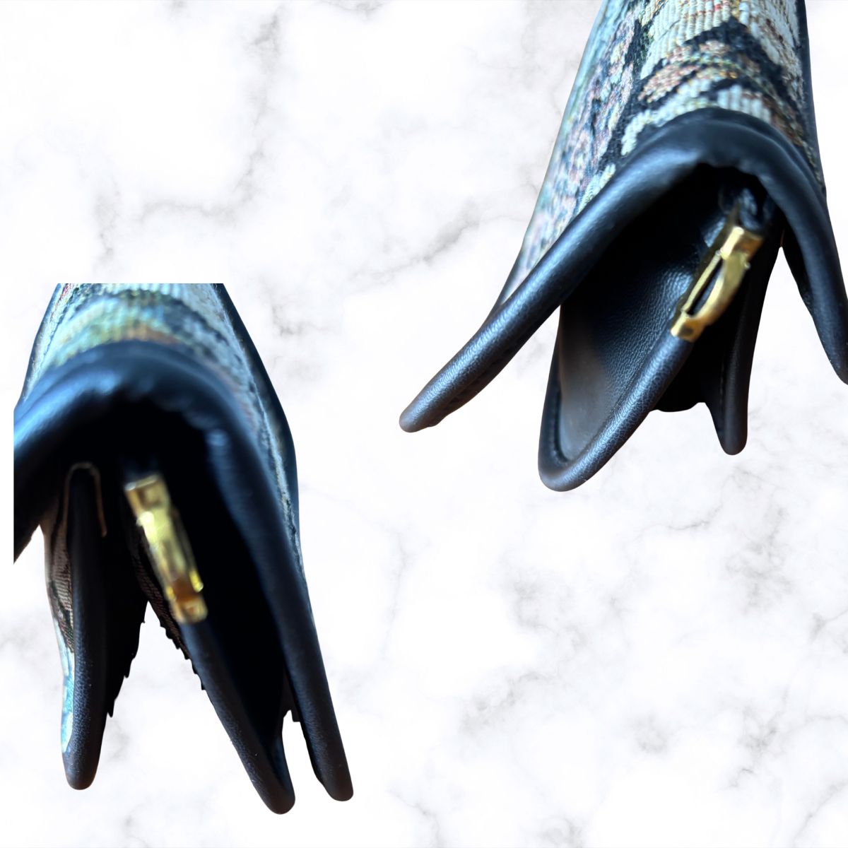 A close-up of a handbag corners on each side showing a black leather tip with a gold-tone clasp, set against a white marble background.