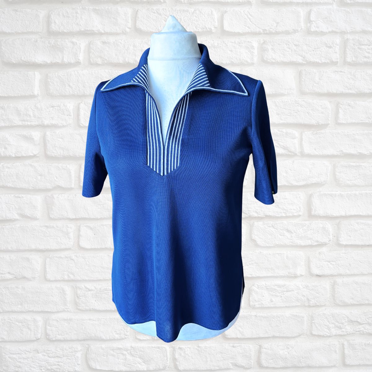 Blue short-sleeve shirt with striped collar on a mannequin against a white brick wall.