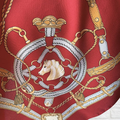 Close-up of a red fabric with gold, white, and beige equestrian-themed design.