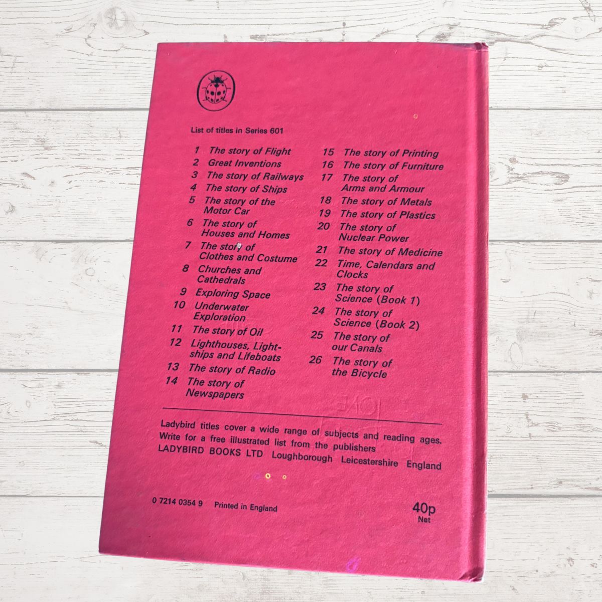 A pink hardcover book lying flat on a white wood surface, showing the back cover with a printed list of included stories and publisher details.