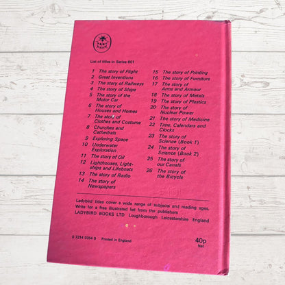 A pink hardcover book lying flat on a white wood surface, showing the back cover with a printed list of included stories and publisher details.