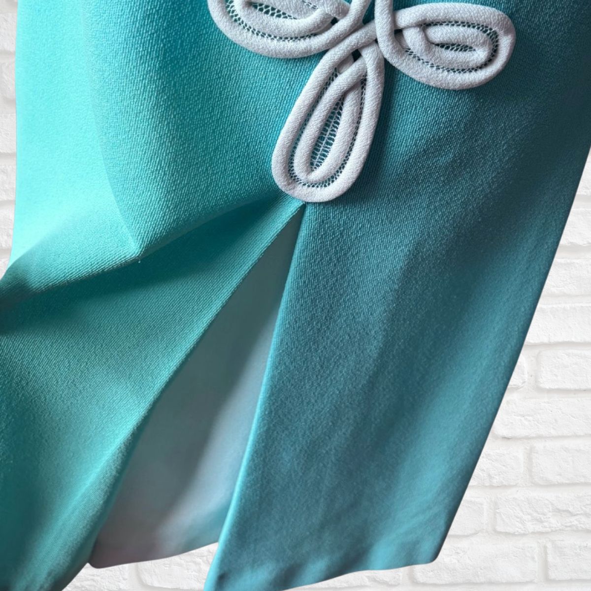 Close-up of a turquoise fabric with a decorative bow on a textured white background