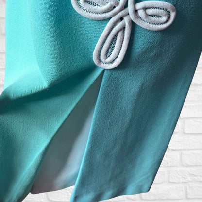 Close-up of a turquoise fabric with a decorative bow on a textured white background