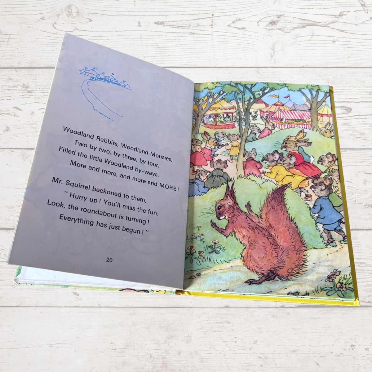 An open children's book spread on a light wood surface, showing a printed poem on the left page and a colorful woodland illustration with animals on the right page.