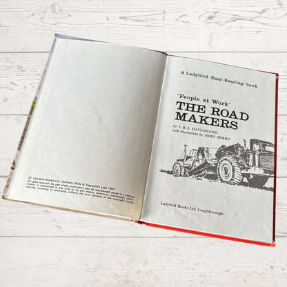 Open book titled 'The Road Makers' on a white wooden surface