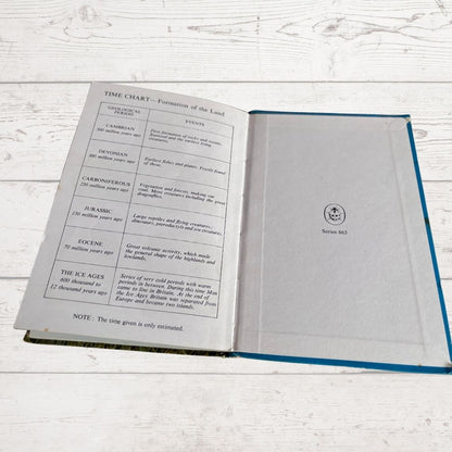 An open vintage ladybird book showing a time chart about the formation of the land on the left page and a blank cover or inside page on the right, placed on a white wooden surface.
