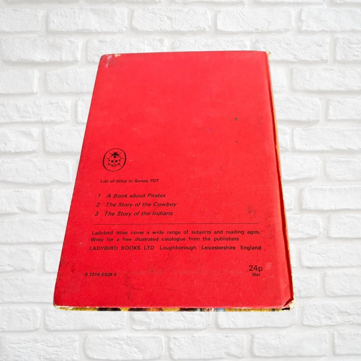 A vintage red hardcover ladybird book on a white painted brick suface 