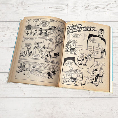 Open comic book titled 'Shiner's Scrapbook' on a wooden surface