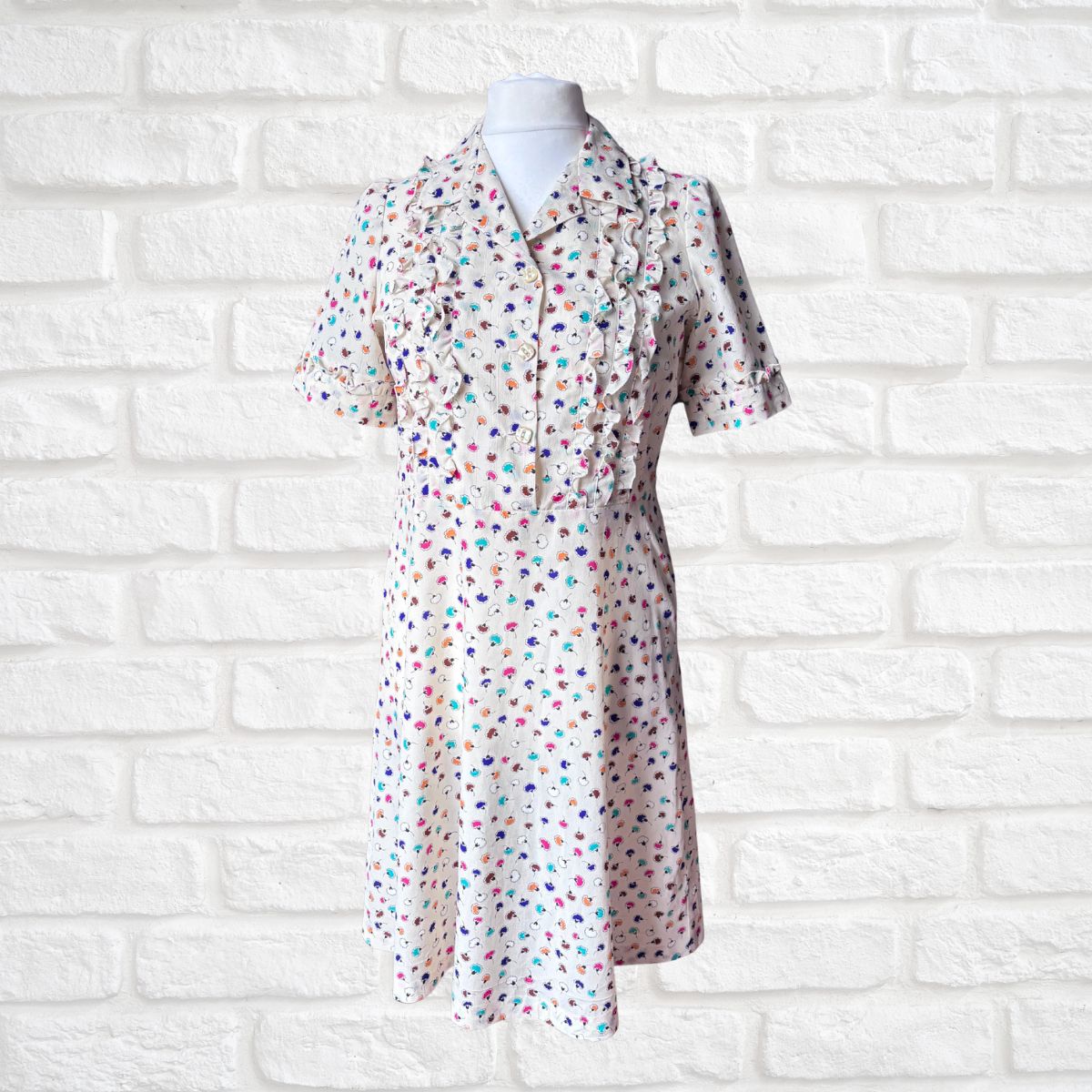 Short-sleeve dress with colorful polka dot pattern on a mannequin against a white brick wall.
