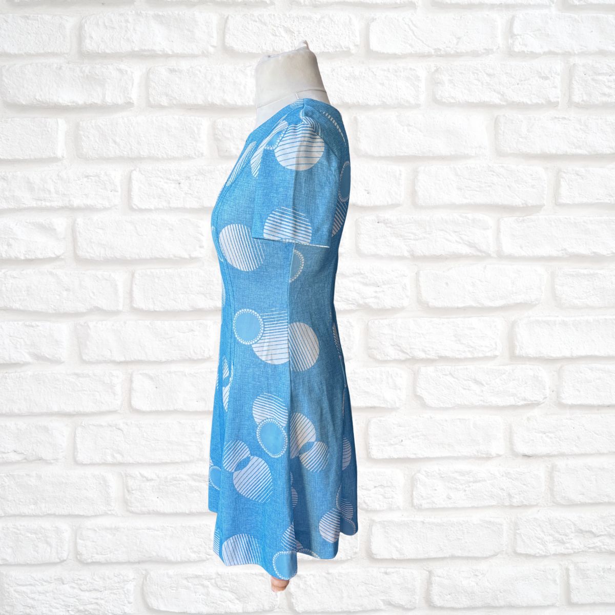 Blue dress with white geometric patterns on a mannequin against a white brick wall.
