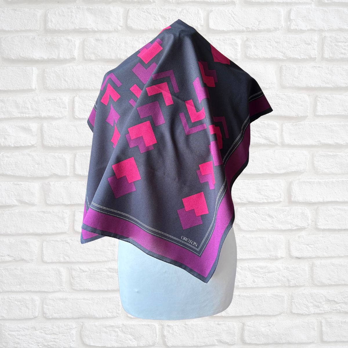 Scarf with pink geometric pattern on a mannequin against a white brick wall
