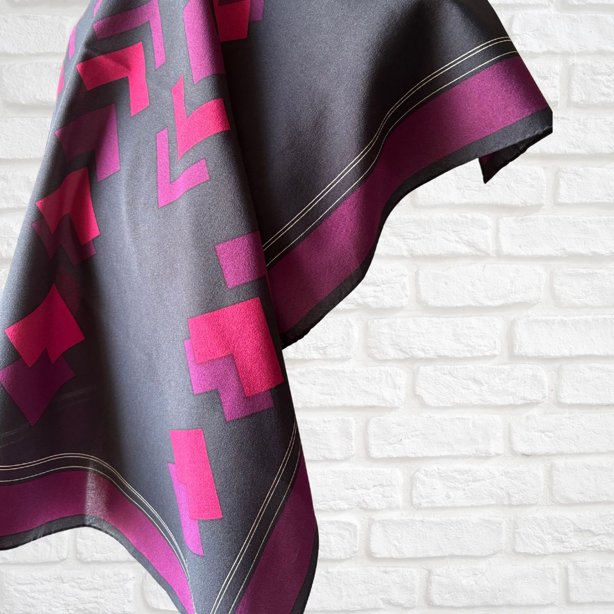 Scarf with pink and purple geometric pattern on a white brick wall background