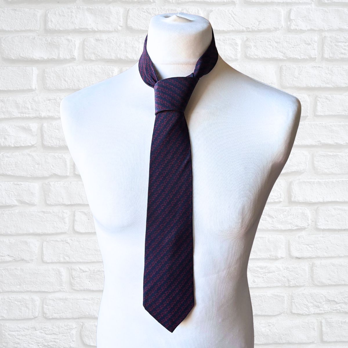 Navy printed tie on a mannequin against a white brick wall background