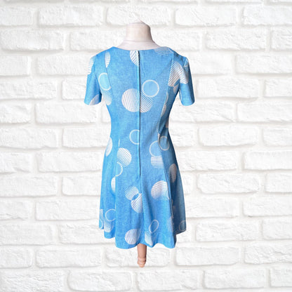 Blue dress with white circular pattern on a mannequin against a white brick wall.