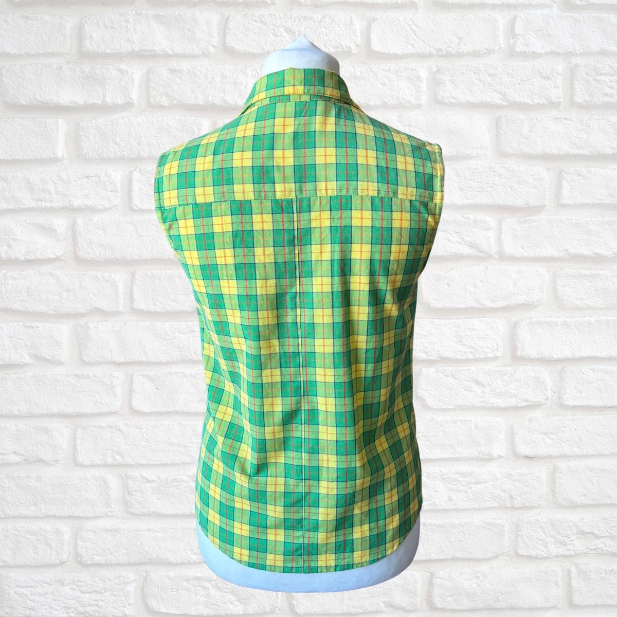 Green and yellow plaid vest on a mannequin against a white brick wall background