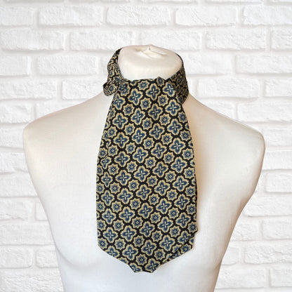 A vintage Austin Reed cravat featuring a black necktie with a cream, gold, and blue abstract floral print, displayed on a mannequin against a white brick wall background.