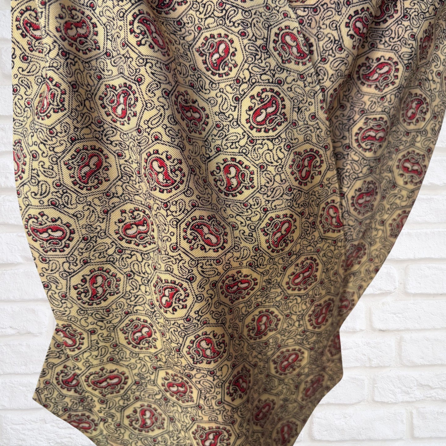 Patterned cravat  with red and gold design on a white brick wall background