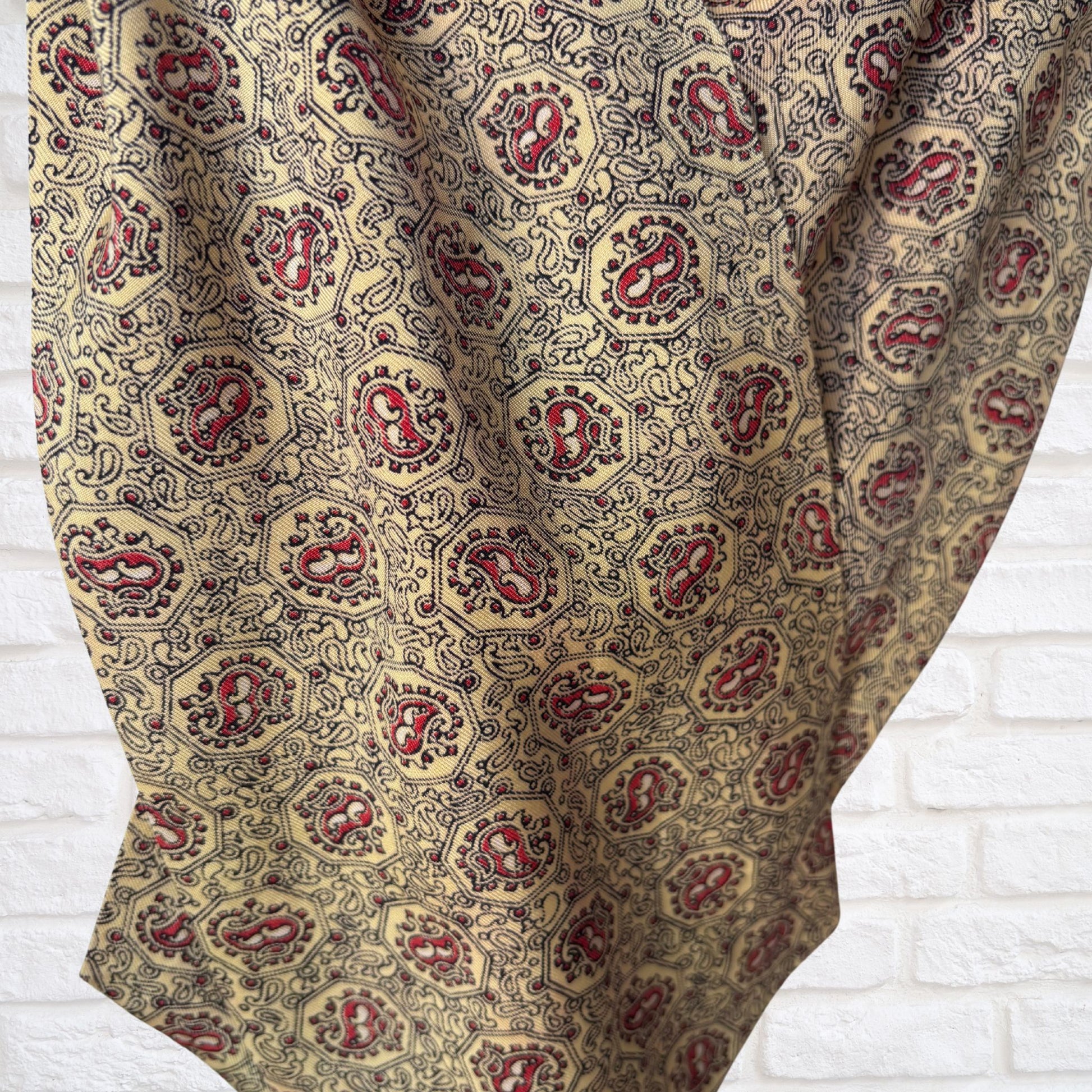 Patterned cravat  with red and gold design on a white brick wall background